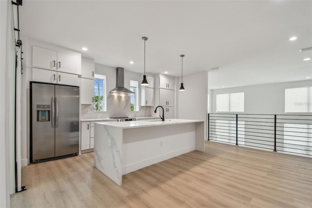 A modern kitchen features white cabinetry, a marble-topped island, stainless steel appliances, and wood flooring — 3826 POMPANO DRIVE SE, ST PETERSBURG, FL