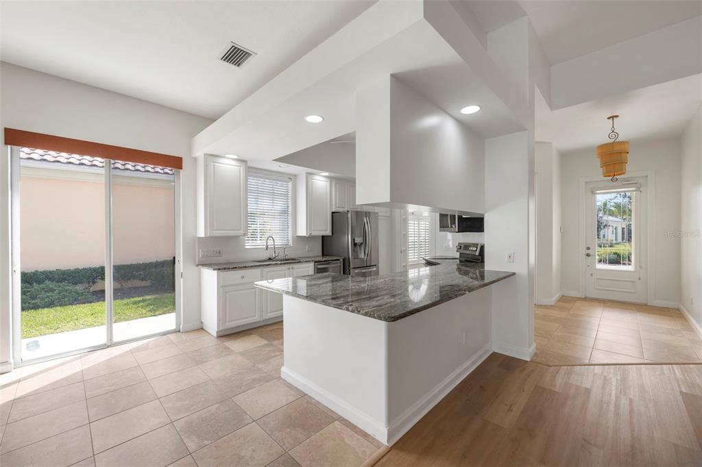 A kitchen with white cabinets, granite countertops, and tile flooring next to a sliding glass door — 5779 WILENA PLACE, SARASOTA, FL