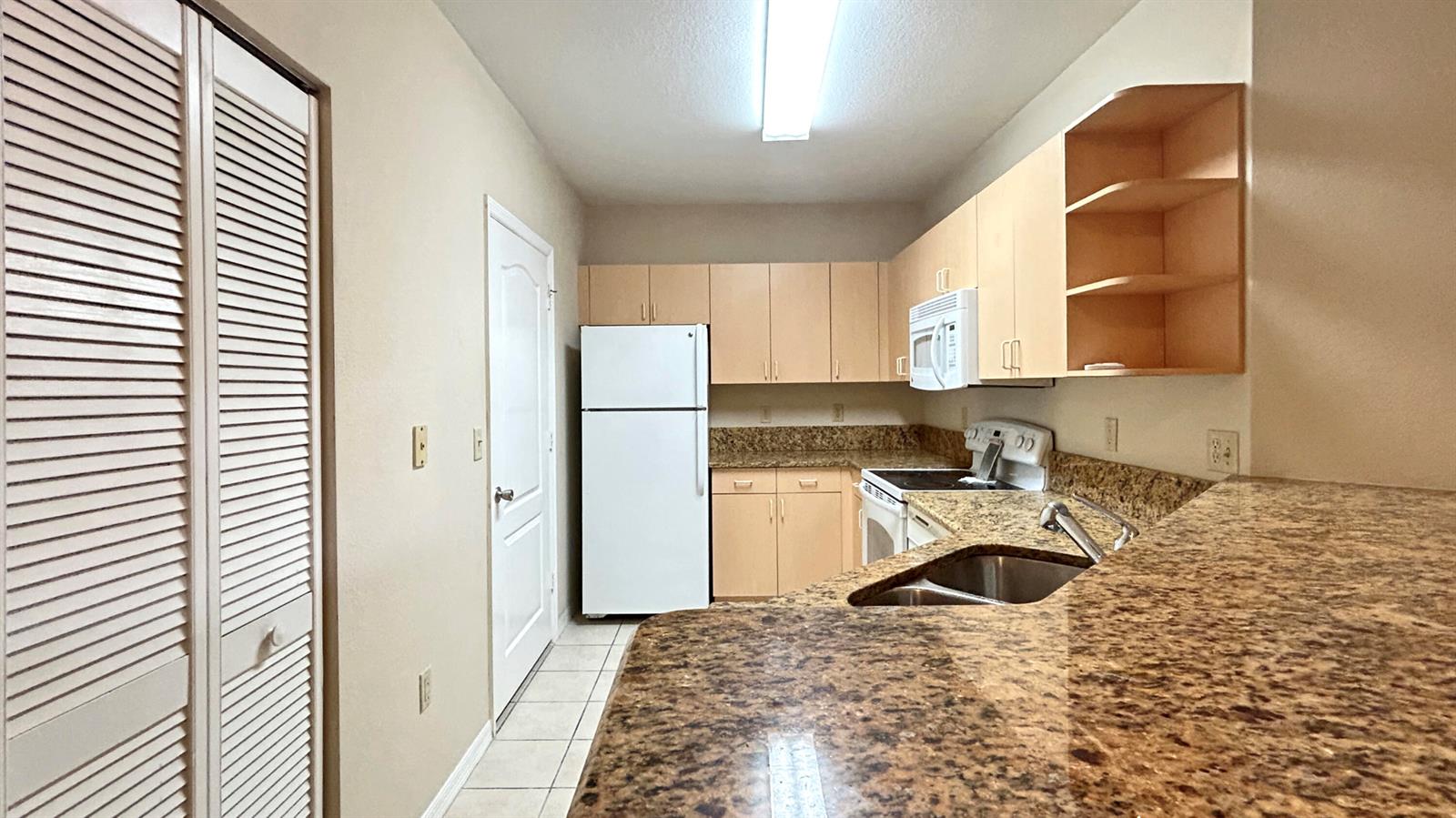 A kitchen features light wood cabinets, granite countertops, a white refrigerator, and a stainless sink — 104 SW Peacock Boulevard # 204, FL 34986, FL