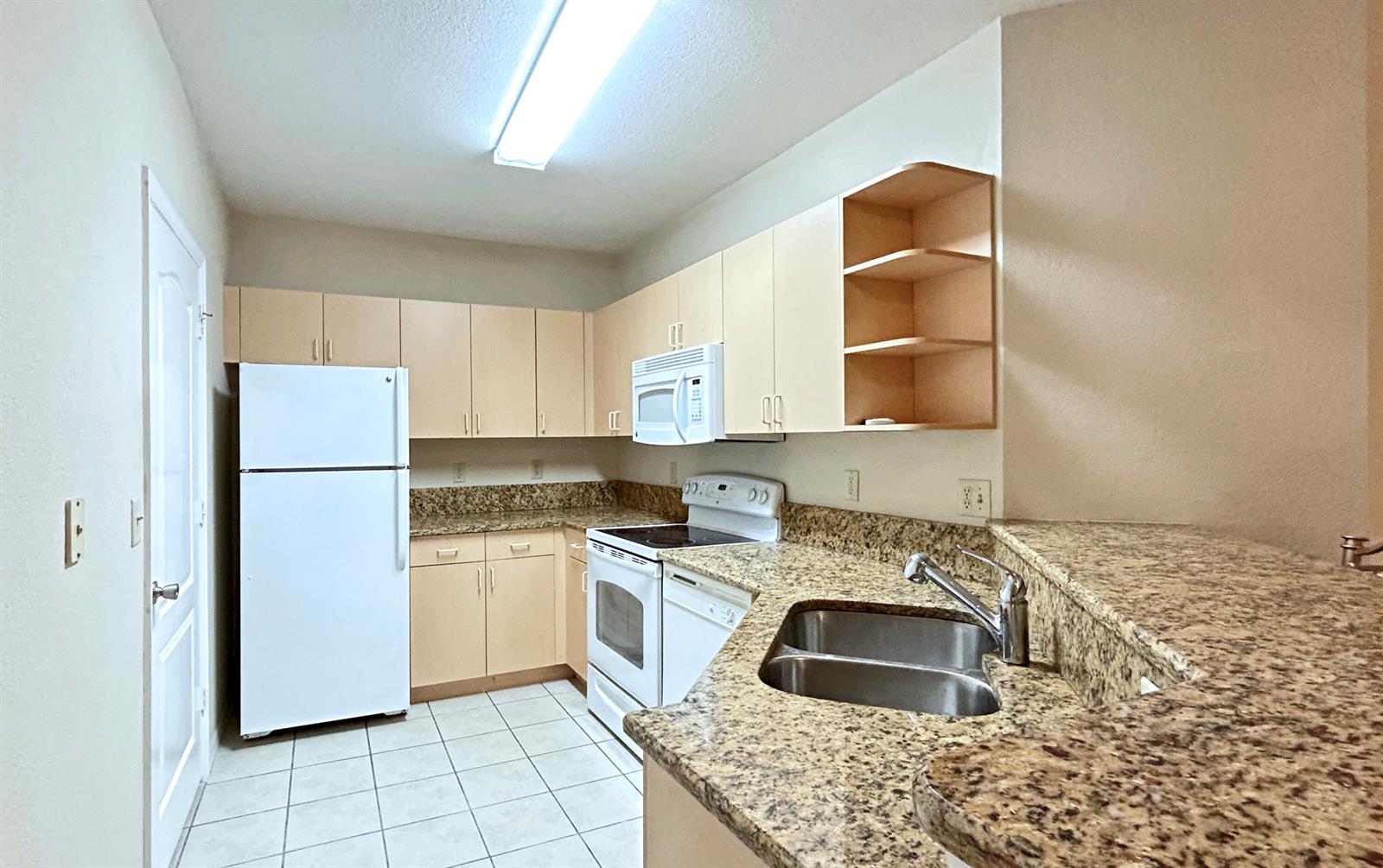 A kitchen features light wood cabinets, granite countertops, white appliances, and a double-basin sink — 104 SW Peacock Boulevard # 204, FL 34986, FL
