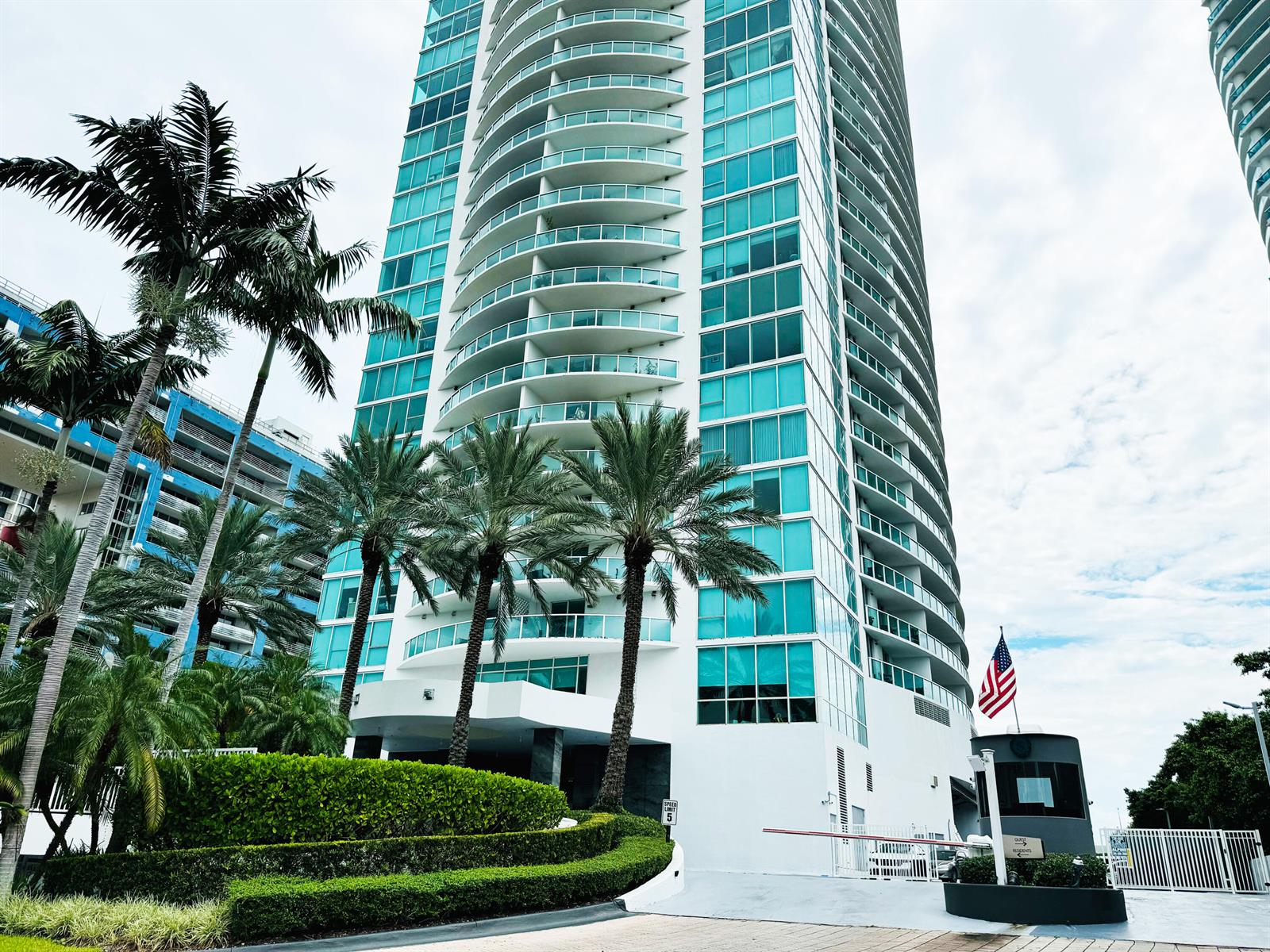 A tall, curved glass residential high-rise building stands behind a landscaped entrance with palm trees — 2101 Brickell Avenue # 801, Miami FL 33129, MIAMI, FL