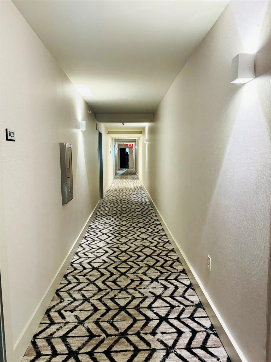 A long hotel hallway features patterned carpeting, light-colored walls, and wall-mounted light fixtures — 2101 Brickell Avenue # 801, Miami FL 33129, MIAMI, FL