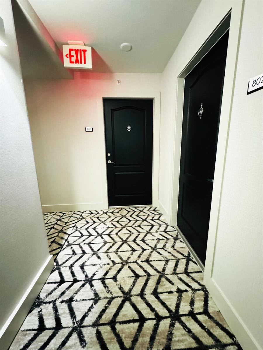 A hallway features patterned carpet, two black doors, and an illuminated exit sign — 2101 Brickell Avenue # 801, Miami FL 33129, MIAMI, FL