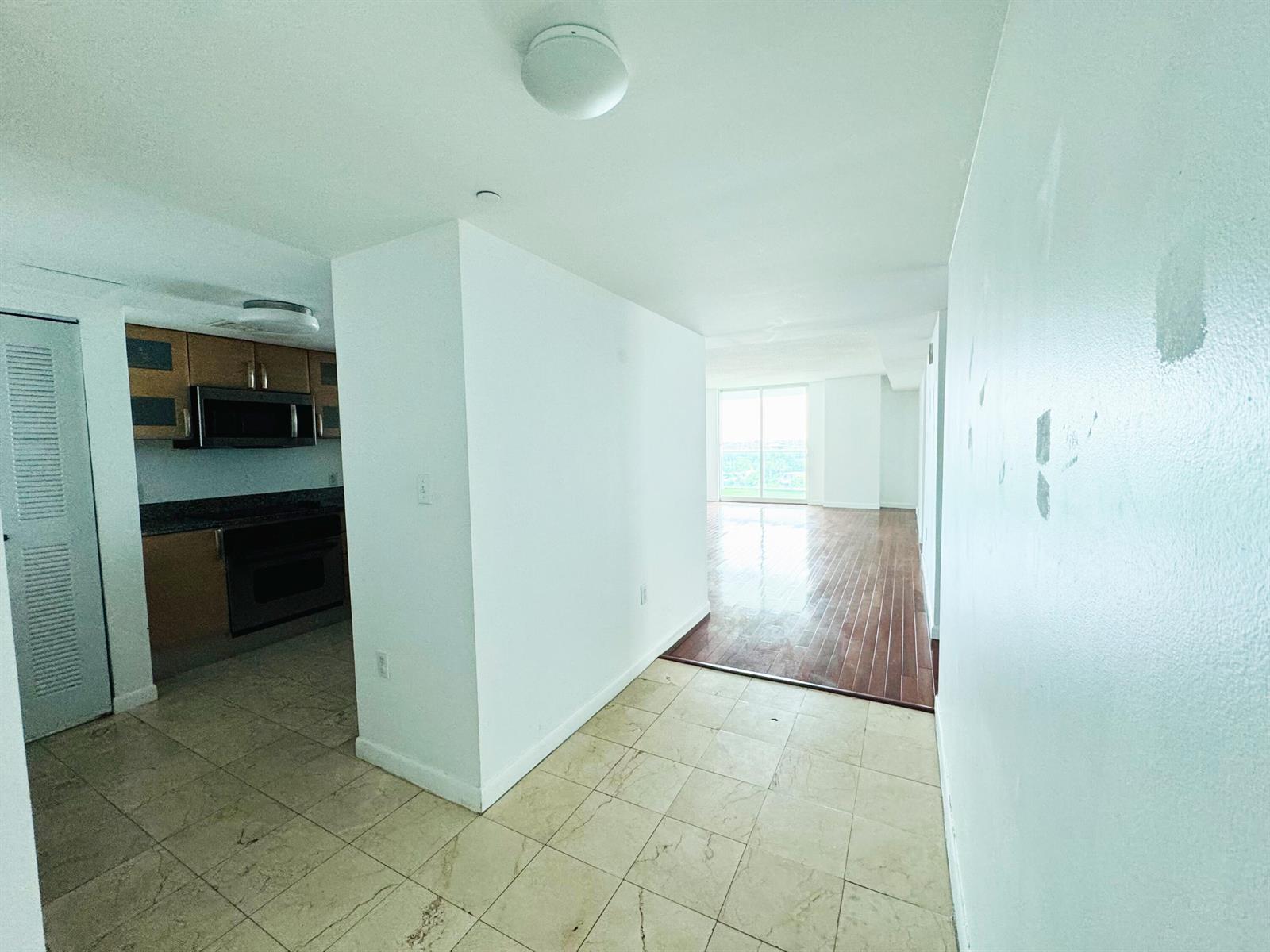 A kitchen with wood cabinets and tile floors transitions into a living area with wood flooring — 2101 Brickell Avenue # 801, Miami FL 33129, MIAMI, FL
