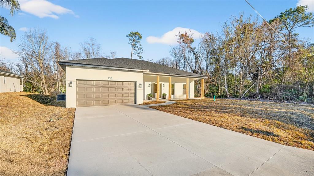 A single-story house with a tan exterior, a two-car garage, and wooden porch columns — 257 LAGO VISTA STREET, DEBARY, FL