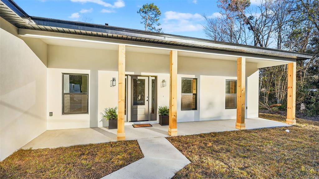 A modern house exterior features a covered porch with light wood posts and white walls — 257 LAGO VISTA STREET, DEBARY, FL
