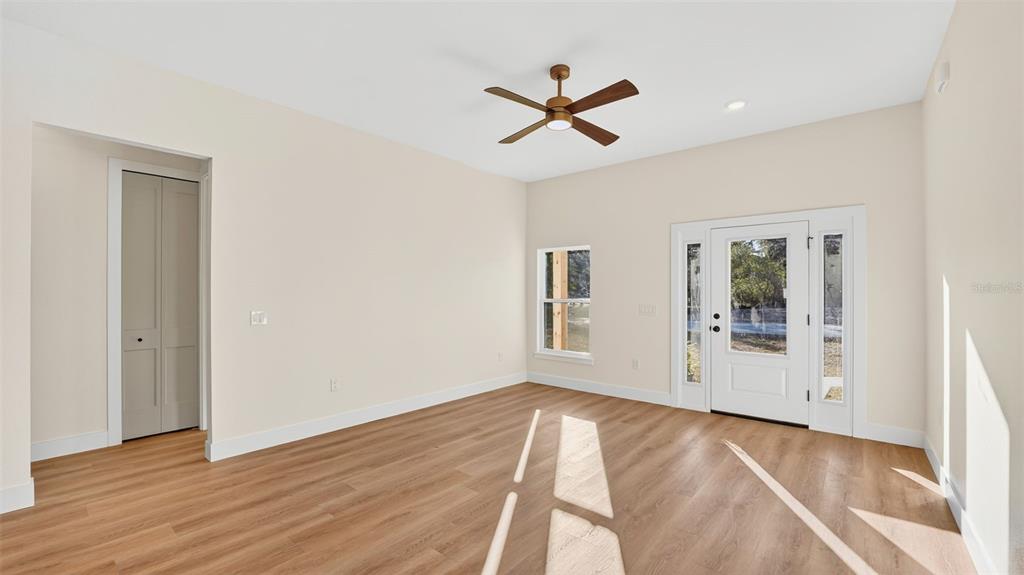An empty room features light wood flooring, beige walls, a ceiling fan, and a front door — 257 LAGO VISTA STREET, DEBARY, FL
