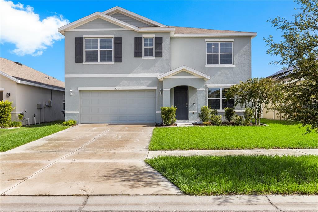 A two-story house with a light gray stucco exterior, a two-car garage, and a lawn — 10212 GOLDEN LIGHT COURT, RIVERVIEW, FL