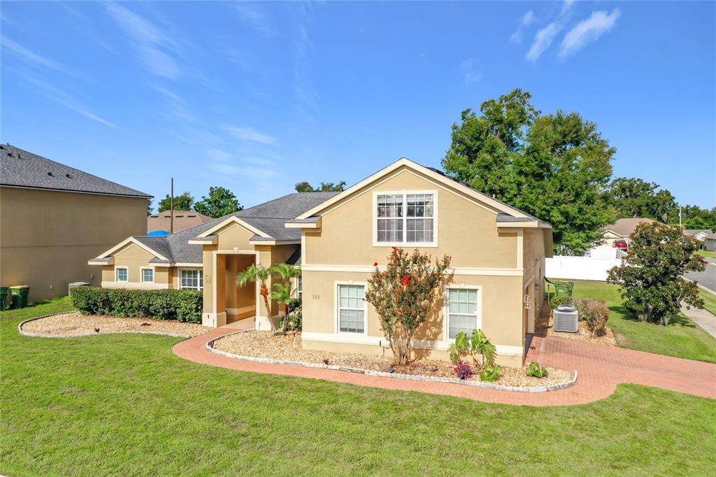 A two-story tan stucco house with a red brick walkway and a front-facing garage — 301 ASHTON WOODS LANE, LEESBURG, FL