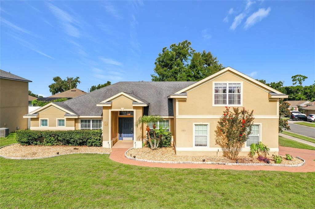A tan, two-story suburban house features a brick walkway, a front lawn, and landscaping — 301 ASHTON WOODS LANE, LEESBURG, FL