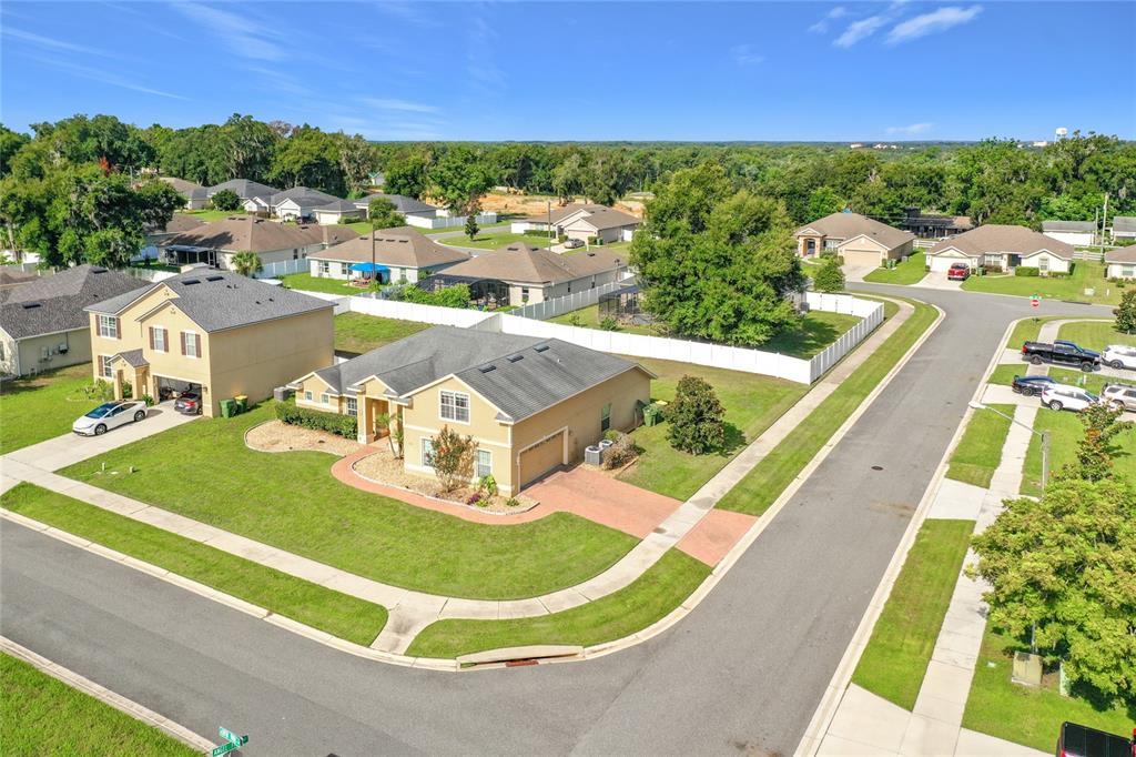 An aerial view of a suburban corner lot featuring a tan single-family home with landscaping — 301 ASHTON WOODS LANE, LEESBURG, FL