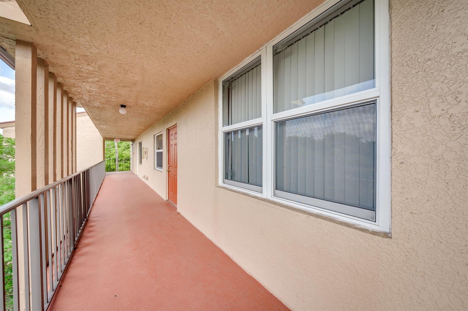 An outdoor apartment walkway features a red floor, a metal railing, and a brown door — 7301 NW 1st Street # 402, Margate FL 33063, MARGATE, FL
