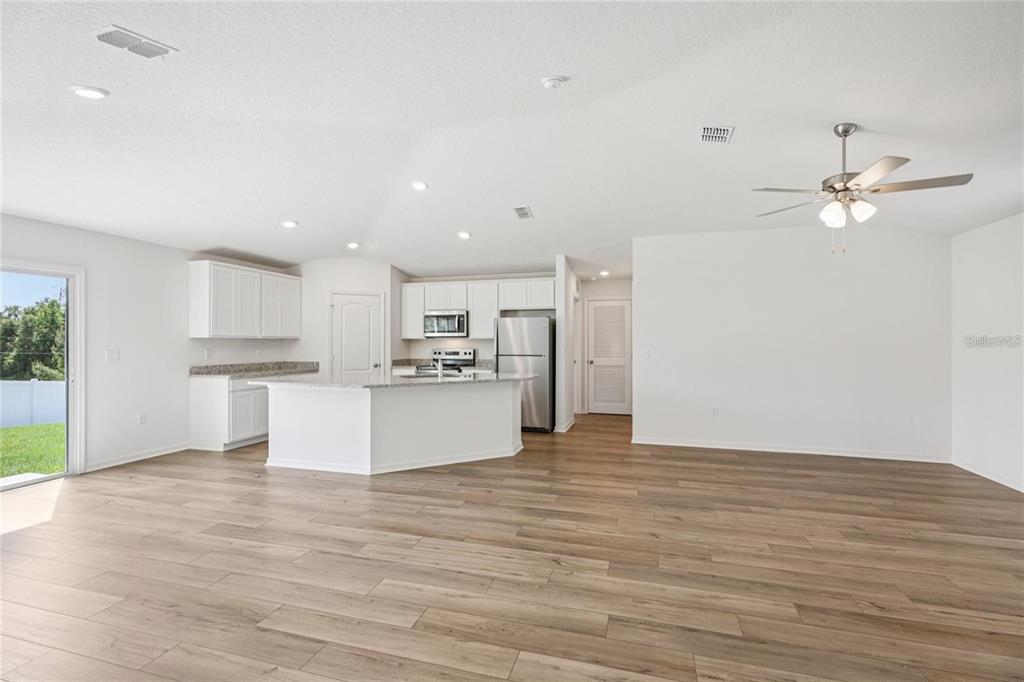 A bright open-concept kitchen and living area features white cabinetry, stainless appliances, and wood-look flooring — 16984 SW 40 CIRCLE, OCALA, FL