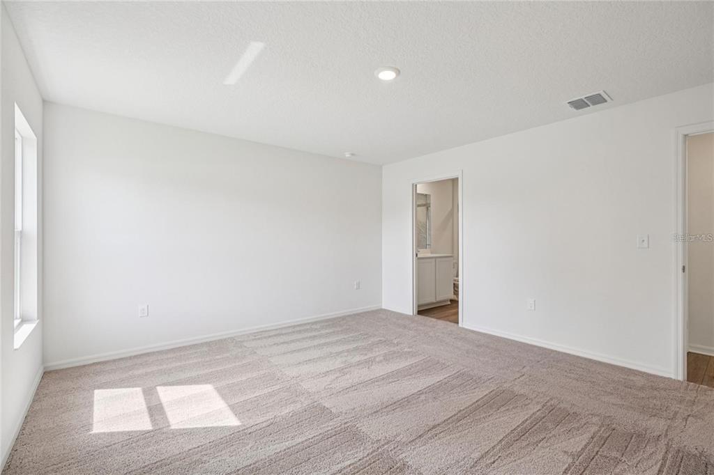 An empty bedroom features beige carpet, white walls, a recessed light, and an attached bathroom — 16984 SW 40 CIRCLE, OCALA, FL