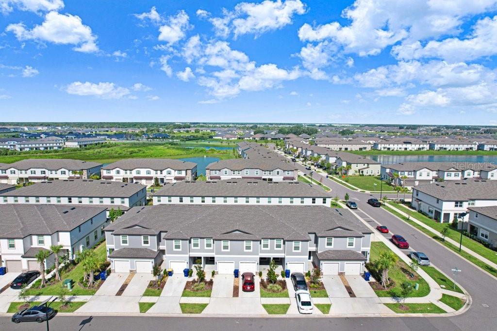 An aerial view shows multiple rows of modern townhouses with driveways and a nearby pond — 10263 TRUMPET HONETSUCKLE WAY, SAN ANTONIO, FL