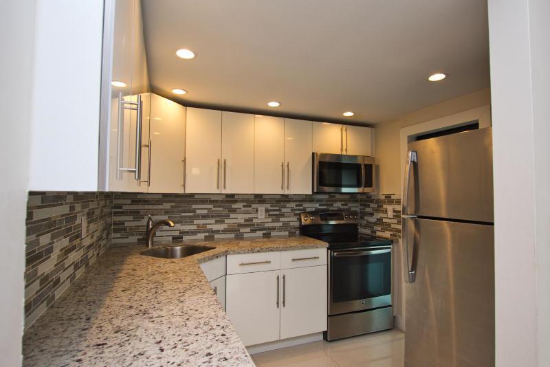 A kitchen with white cabinets, granite countertops, stainless steel appliances, and a mosaic tile backsplash — 300 80th Street, Miami Beach FL 33141, MIAMI BEACH, FL