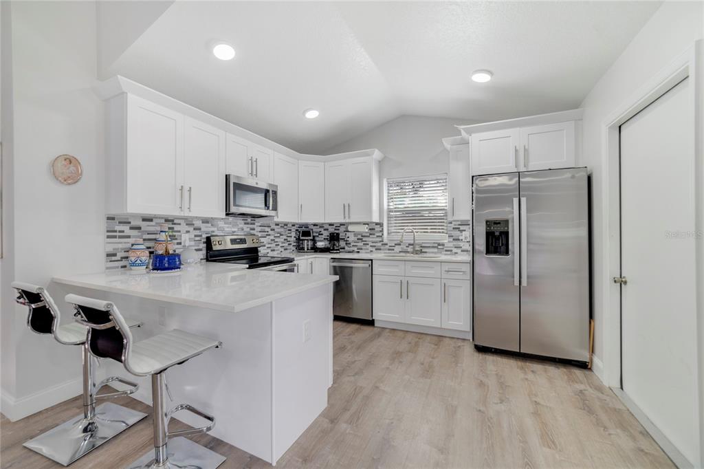 A modern kitchen features white cabinets, stainless steel appliances, a breakfast bar, and wood-look flooring — 1104 W 3RD STREET, SANFORD, FL