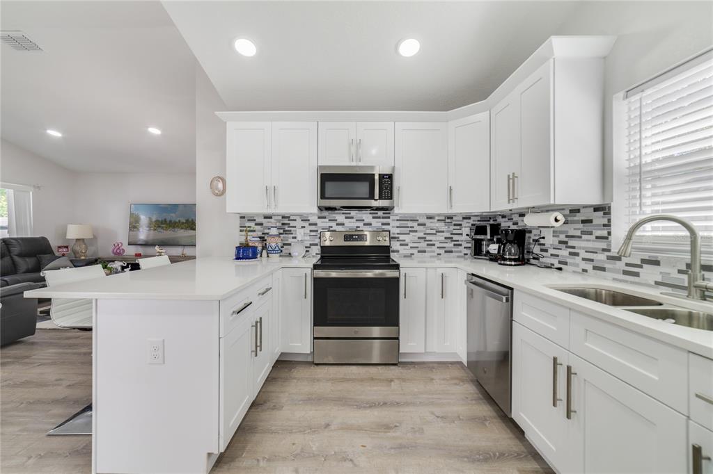 A modern kitchen features white cabinets, stainless steel appliances, and a gray tiled backsplash — 1104 W 3RD STREET, SANFORD, FL