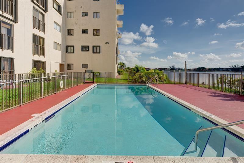 A rectangular swimming pool sits next to a multi-story building overlooking a lake — 9915 W Okeechobee Rd # 404, Hialeah Gardens FL 33016, HIALEAH GARDENS, FL