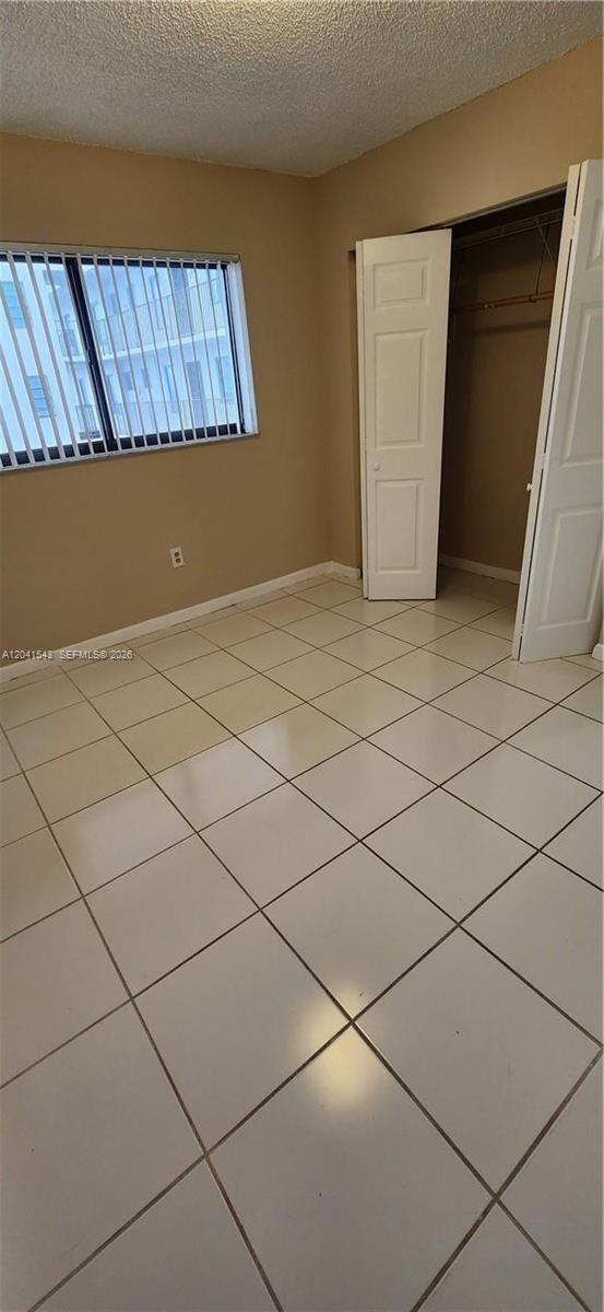An empty bedroom features beige walls, white tile flooring, a window with blinds, and a closet — 9915 W Okeechobee Rd # 404, Hialeah Gardens FL 33016, HIALEAH GARDENS, FL