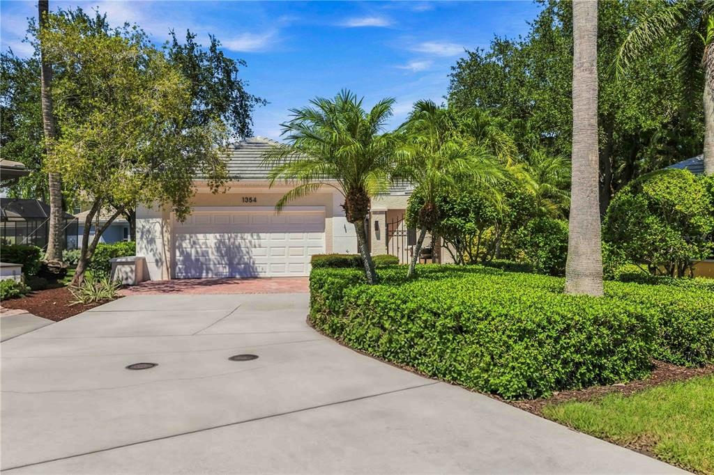 A single-story house with a white garage door, concrete driveway, and lush landscaping — 1354 TEAROSE PLACE, SARASOTA, FL