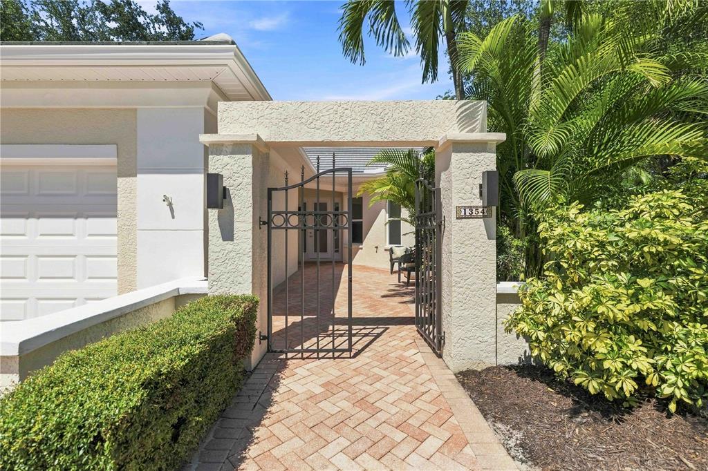 A gated brick walkway leads to the front entrance of a stucco home — 1354 TEAROSE PLACE, SARASOTA, FL