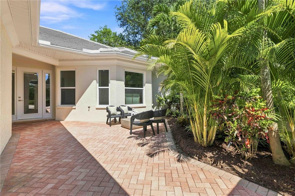 A paved patio area features outdoor seating next to a house with palm trees — 1354 TEAROSE PLACE, SARASOTA, FL