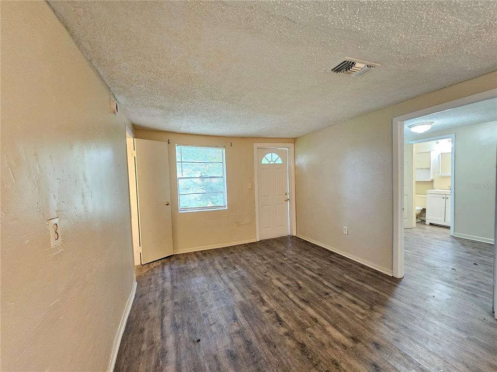 A living room with wood-look flooring, a window, a white door, and an adjacent bathroom — 1504 E 99TH AVENUE UNIT B, TAMPA, FL