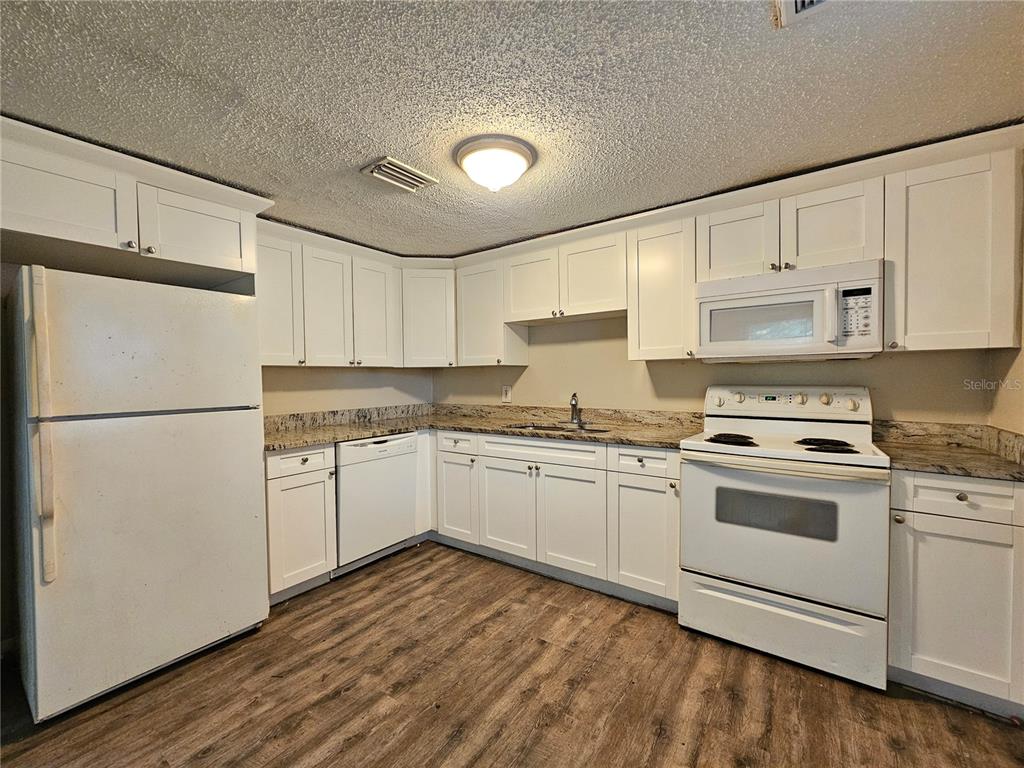 A kitchen with white cabinets, granite countertops, white appliances, and wood-look flooring — 1504 E 99TH AVENUE UNIT B, TAMPA, FL