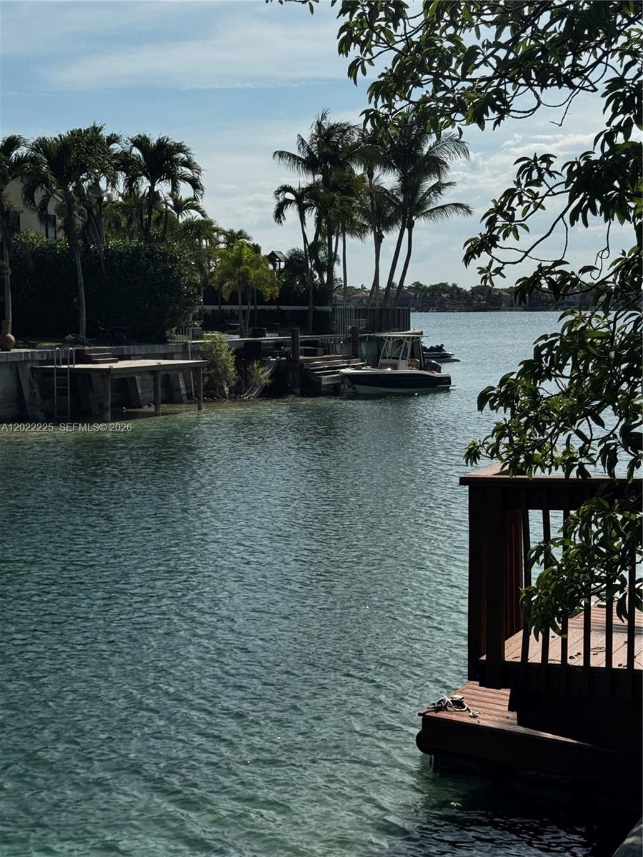 A wooden deck overlooks a canal with a boat docked near palm trees — 13312 SW 144th Ter, Miami FL 33186, MIAMI, FL