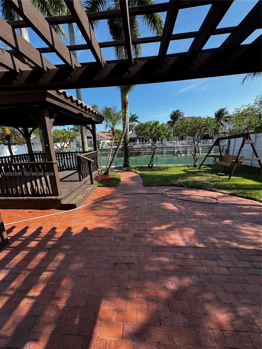 A brick patio features a wooden gazebo and a swing set overlooking a canal — 13312 SW 144th Ter, Miami FL 33186, MIAMI, FL