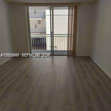 An empty room with light wood-look flooring and a sliding glass door leading to a balcony — MIAMI BEACH, FL