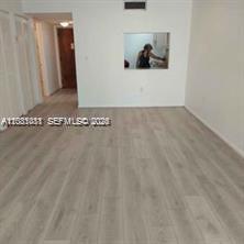 An empty room with light wood-look flooring and a pass-through window to the kitchen — MIAMI BEACH, FL
