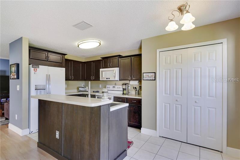 A kitchen features dark wood cabinets, white appliances, a breakfast bar, and white tile flooring — 8008 SUTTON TERRACE LANE, TAMPA, FL