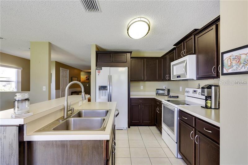 A kitchen features dark wood cabinets, white countertops, a double sink, and stainless steel appliances — 8008 SUTTON TERRACE LANE, TAMPA, FL