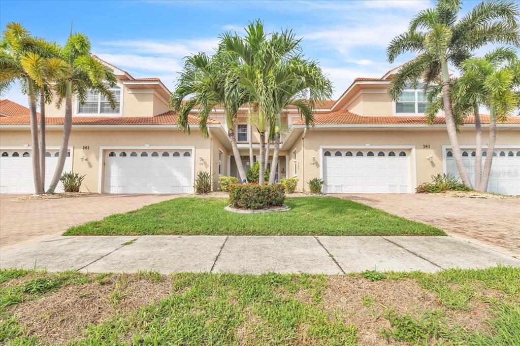 A two-story townhouse exterior with white garage doors, palm trees, and a paved driveway — 141 TROPICANA DRIVE UNIT 1112, PUNTA GORDA, FL