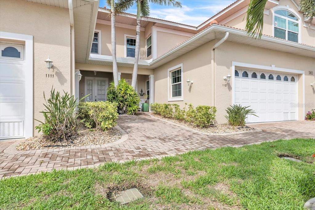 The exterior of a two-story beige house features a brick walkway and two garage doors — 141 TROPICANA DRIVE UNIT 1112, PUNTA GORDA, FL