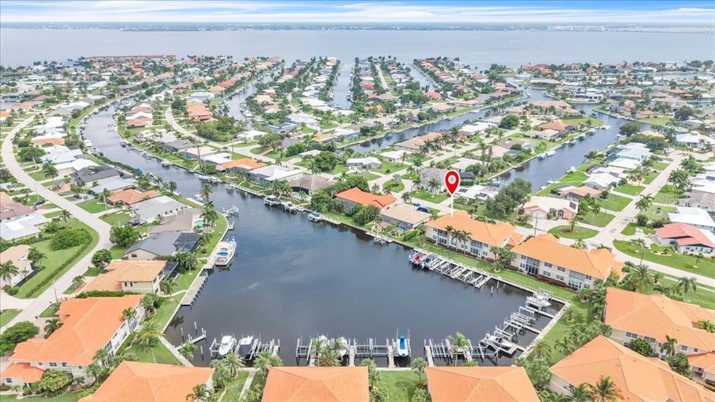 An aerial view shows a waterfront residential complex with boat slips and a red location pin — 141 TROPICANA DRIVE UNIT 1112, PUNTA GORDA, FL