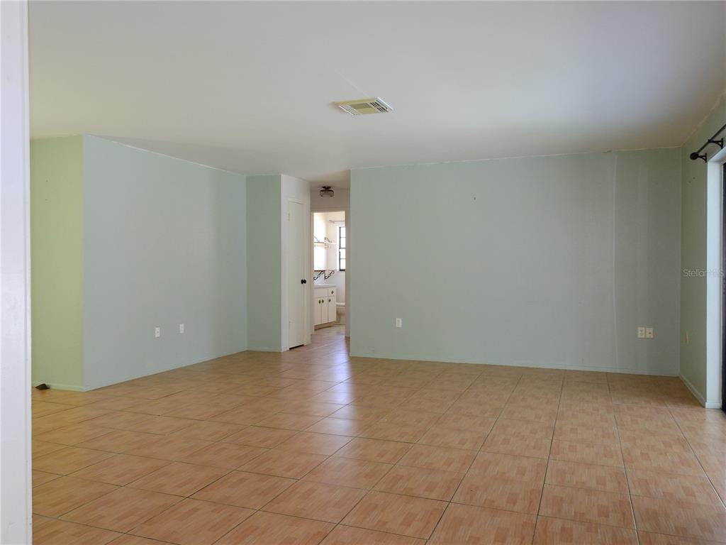 An empty room with light green walls and tan tiled flooring leads to a bathroom — 2128 LINWOOD AVENUE, SPRING HILL, FL