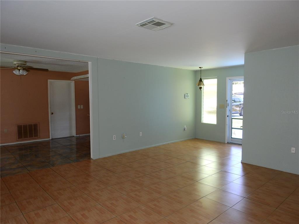 An open-concept living area features light green walls, tiled flooring, and a glass-paned exterior door — 2128 LINWOOD AVENUE, SPRING HILL, FL