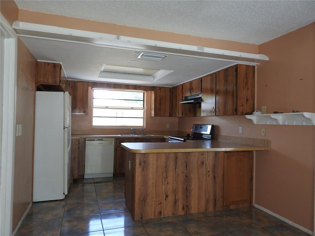 A kitchen with wood-grain cabinets, a white refrigerator, a dishwasher, and tiled flooring — 2128 LINWOOD AVENUE, SPRING HILL, FL