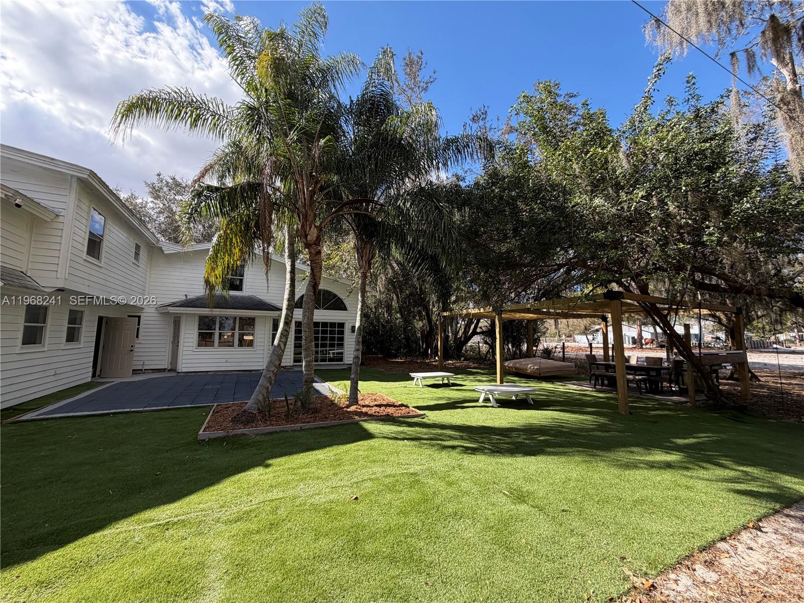 A white house with a patio and artificial turf yard features palm trees and a pergola — 4120 Palomino Dr, Sebring FL 33875, SEBRING, FL