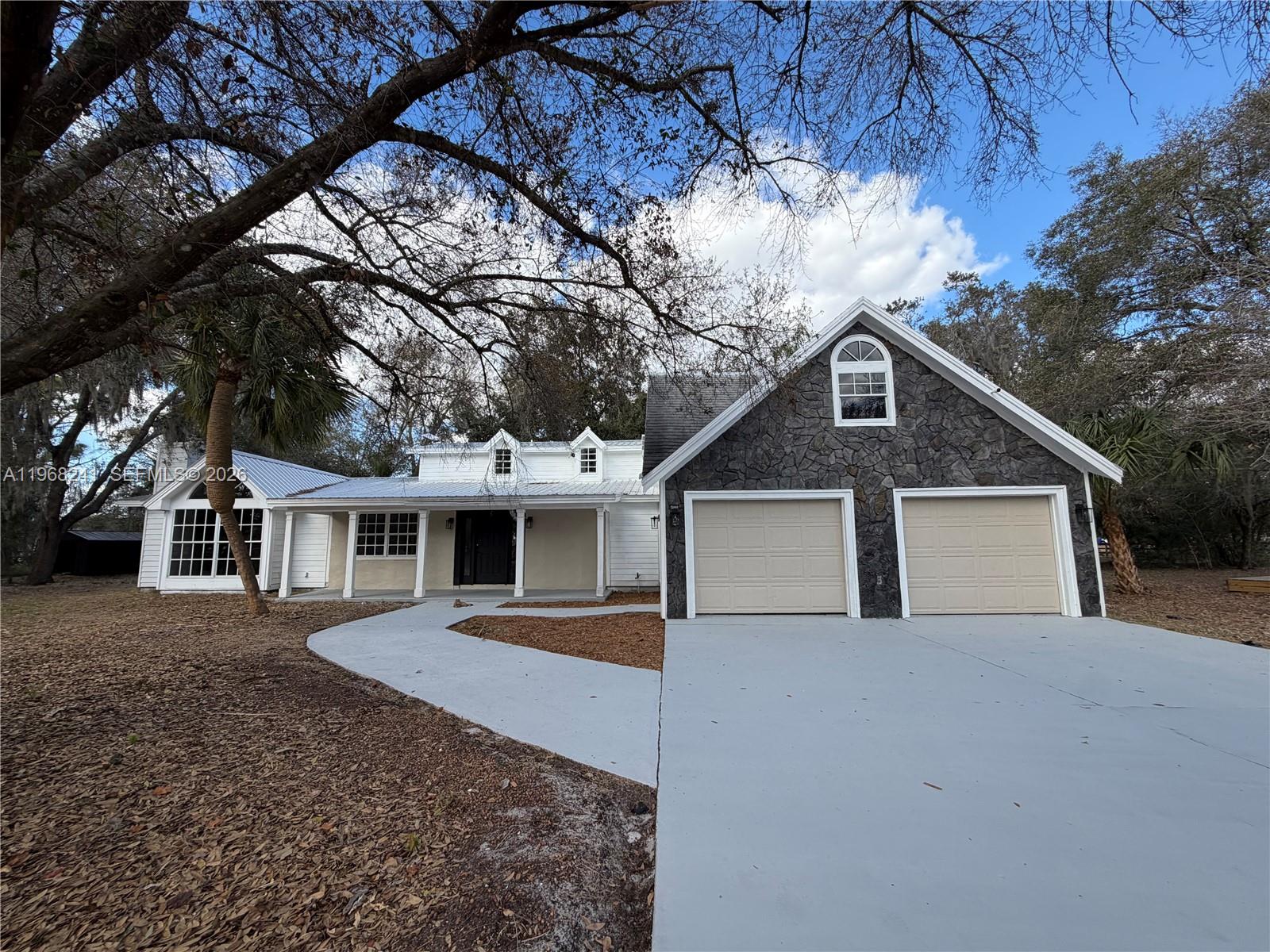 A white house with a stone-faced garage and a curved walkway under large trees — 4120 Palomino Dr, Sebring FL 33875, SEBRING, FL