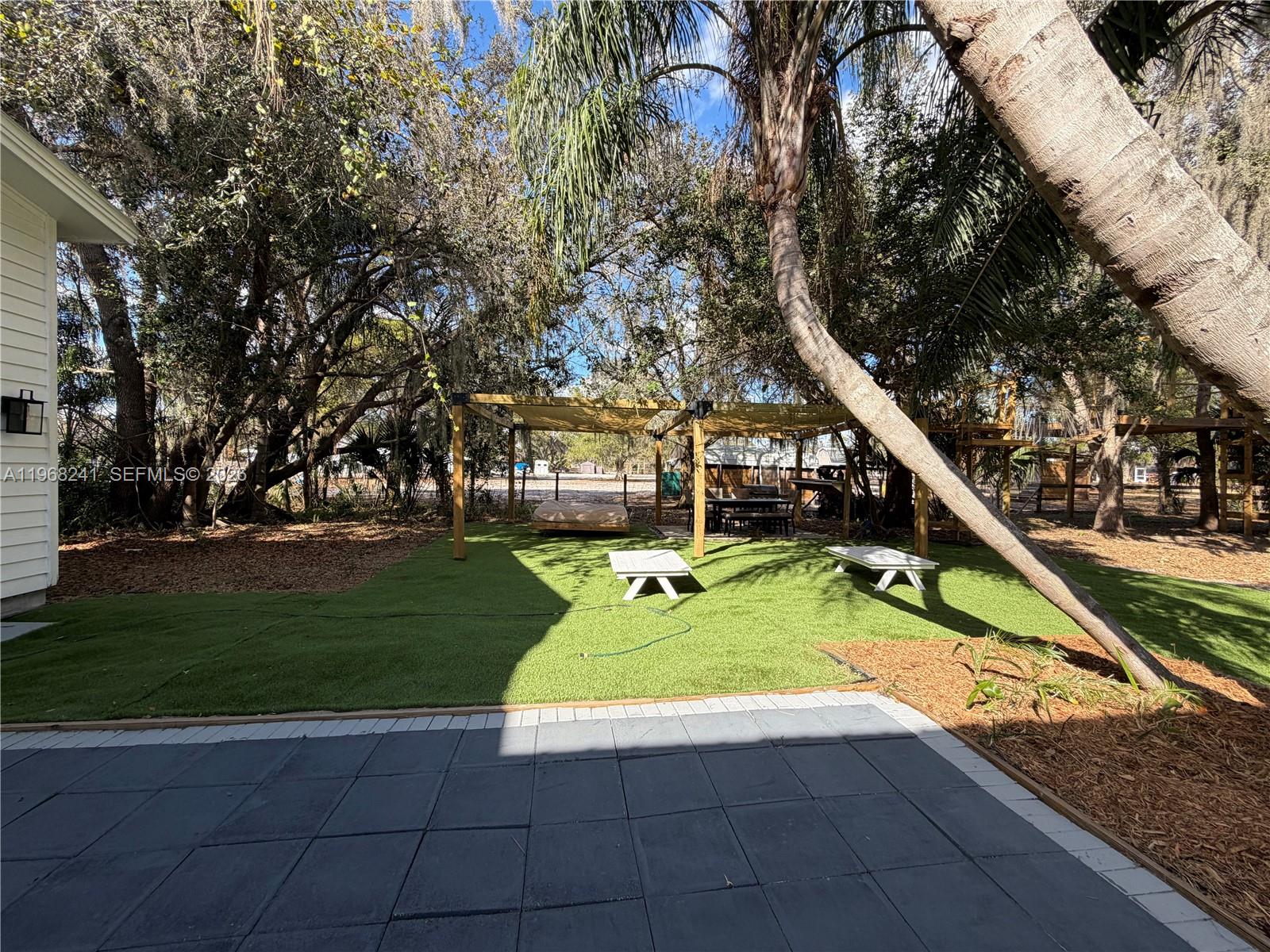 A backyard features artificial turf, a wooden pergola, and a paved patio area — 4120 Palomino Dr, Sebring FL 33875, SEBRING, FL