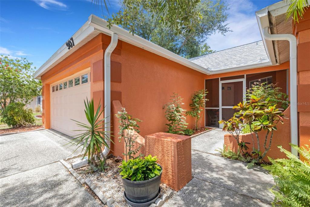 An orange stucco house exterior features a garage, a screened entryway, and landscaped garden beds — 907 50TH STREET E, BRADENTON, FL