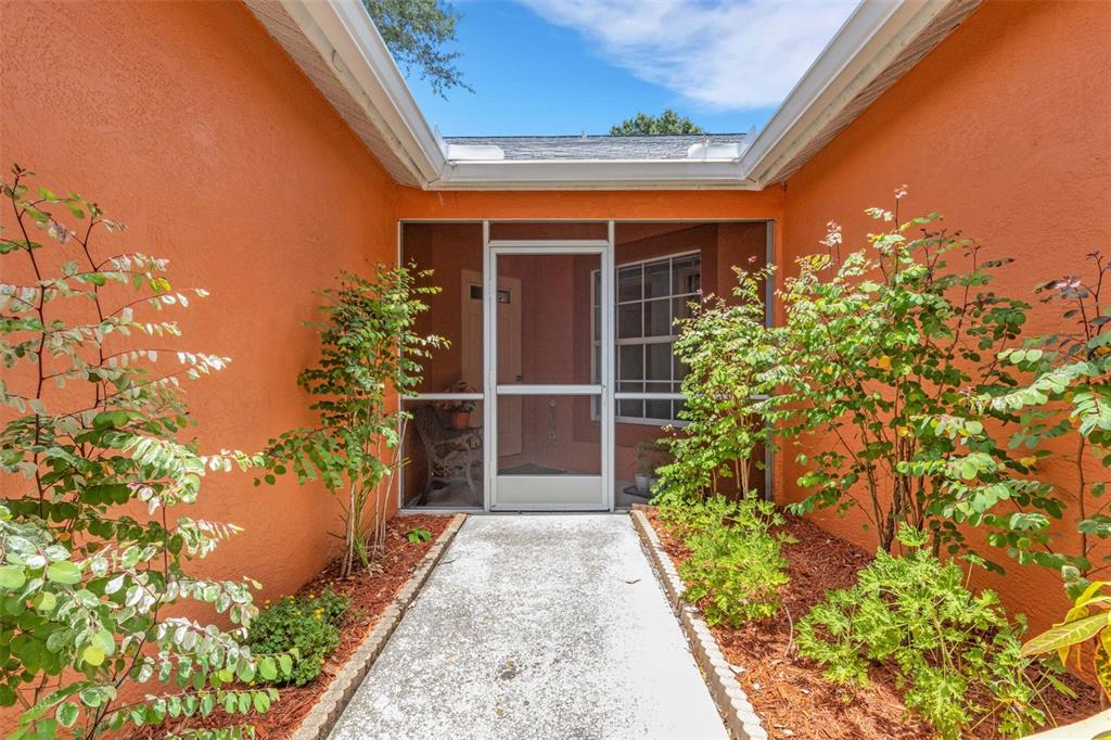 A concrete walkway leads to a screened-in entryway framed by orange stucco walls and landscaping — 907 50TH STREET E, BRADENTON, FL