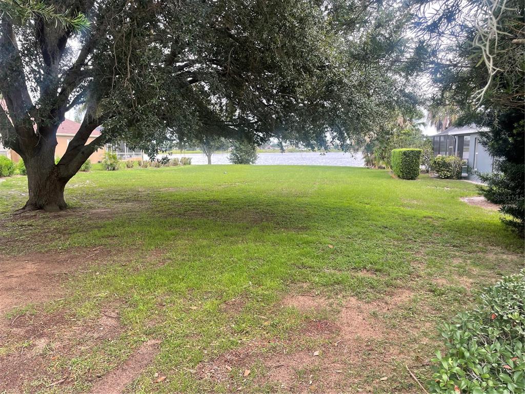 A grassy backyard features a large oak tree and a view of a lake — 348 TERRANOVA BOULEVARD, WINTER HAVEN, FL