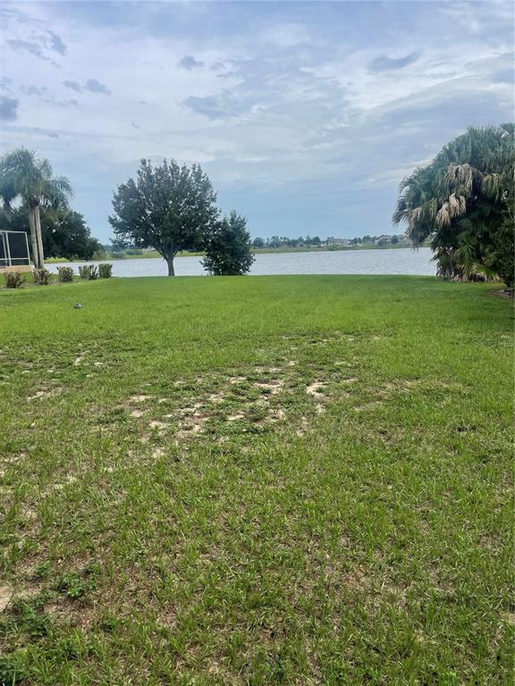 A grassy backyard leads to a lake view with palm trees and a cloudy sky — 348 TERRANOVA BOULEVARD, WINTER HAVEN, FL