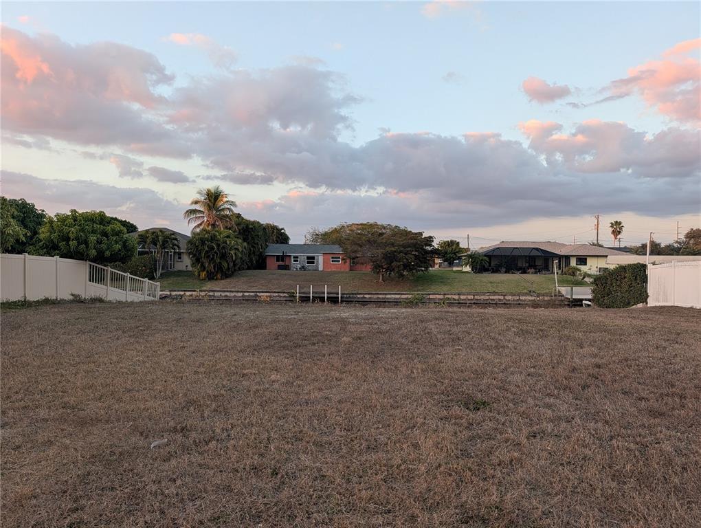 A vacant, grassy lot overlooks a canal with houses in the background under a cloudy sky — 1459 SE 14TH STREET, CAPE CORAL, FL