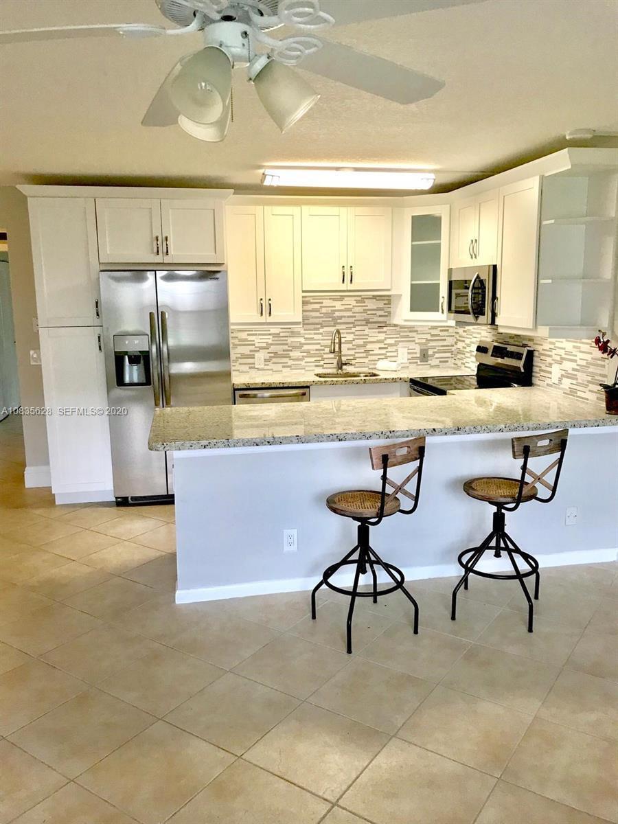 A kitchen features white cabinets, stainless steel appliances, granite countertops, and two bar stools — 86 Mansfield C, Boca Raton FL 33434, BOCA RATON, FL